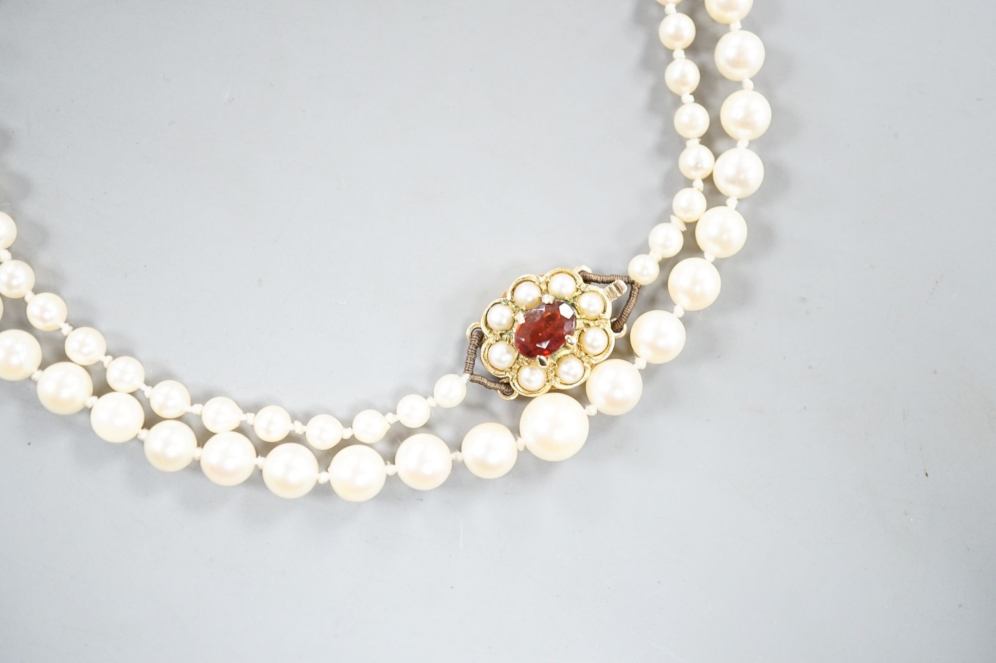 A single strand graduated cultured pearl necklace, with 9ct, garnet and cultured pearl cluster set clasp, 53cm.